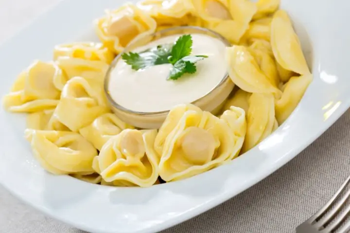 Pyszne pierożki tortellini w sosie śmietanowym, udekorowane natką pietruszki. Idealne danie na szybki obiad.