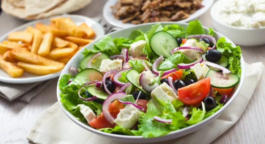 Świeża sałatka gyros z fetą, oliwkami, pomidorami i ogórkiem, obok frytki i mięso gyros.