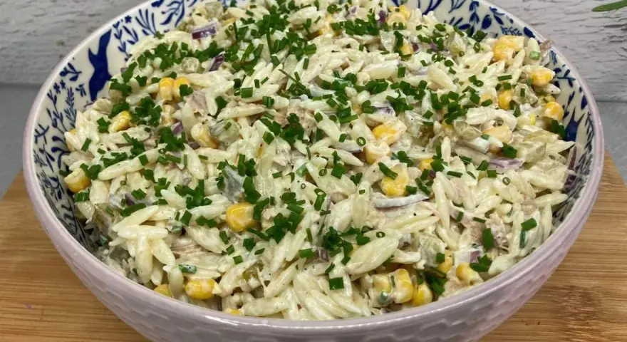 Pyszna sałatka z tuńczykiem, makaronem orzo, kukurydzą i szczypiorkiem, podana w ozdobnej misce.