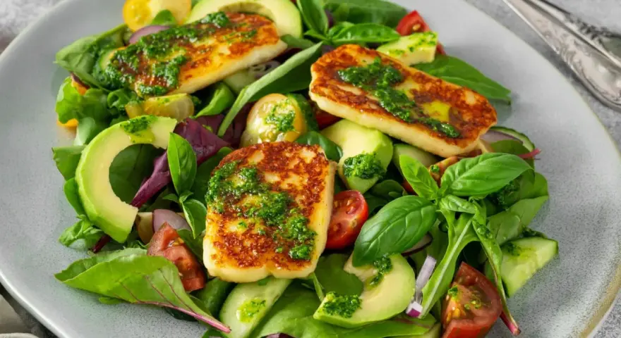 Kolorowa sałatka z grillowanym halloumi, awokado, pomidorkami i ogórkiem, polana zielonym sosem.
