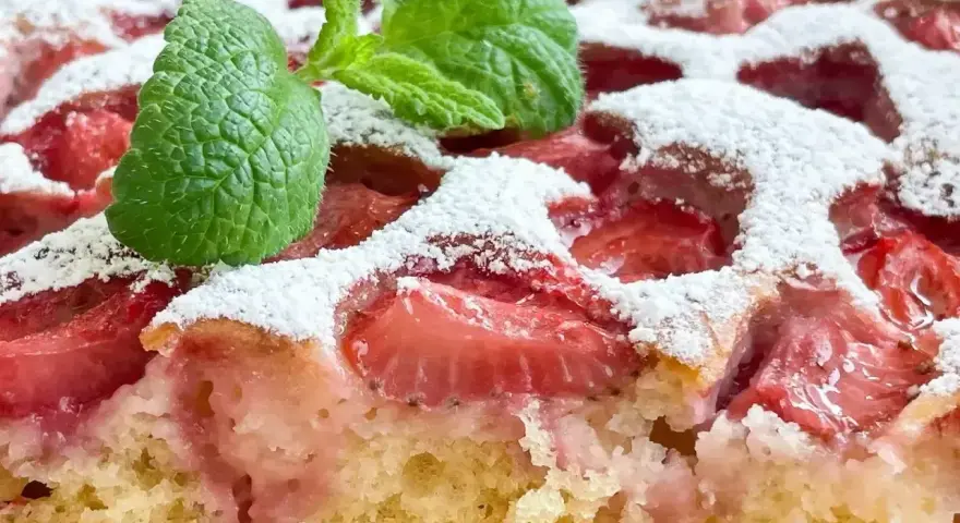 Szybkie ciasto z truskawkami, posypane cukrem pudrem i ozdobione listkiem mięty. Idealne na letnie popołudnie.