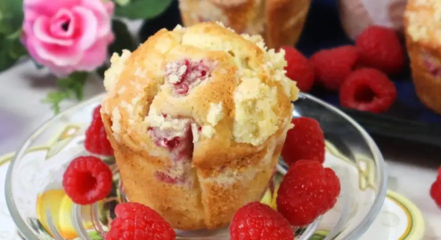 Pyszne muffinki z malinami, posypane kruszonką, otoczone świeżymi malinami.