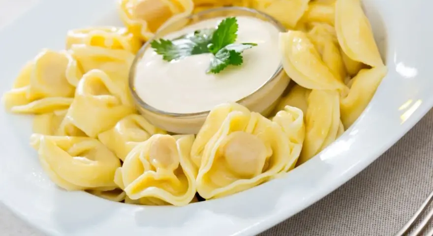 Pyszne pierożki tortellini w sosie śmietanowym, udekorowane natką pietruszki. Idealne danie na szybki obiad.