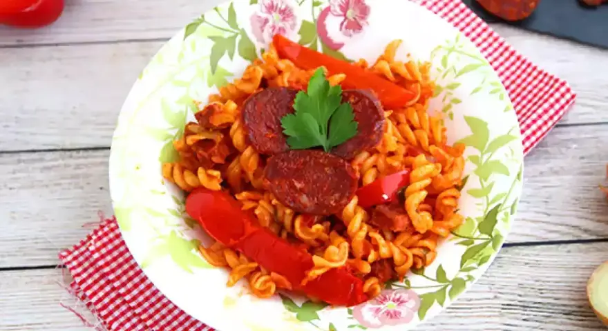 Pyszny makaron z chorizo, papryką i natką pietruszki na talerzu z motywem kwiatowym.