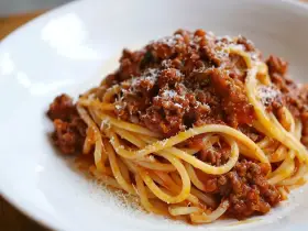 Pyszny sos do makaronu bolognese, obficie polany na spaghetti, posypany parmezanem.