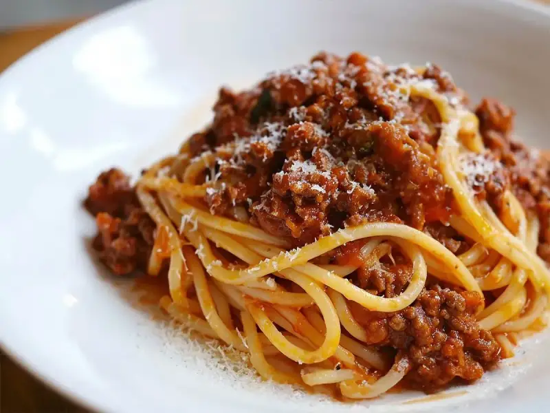 Pyszny sos do makaronu bolognese, obficie polany na spaghetti, posypany parmezanem.