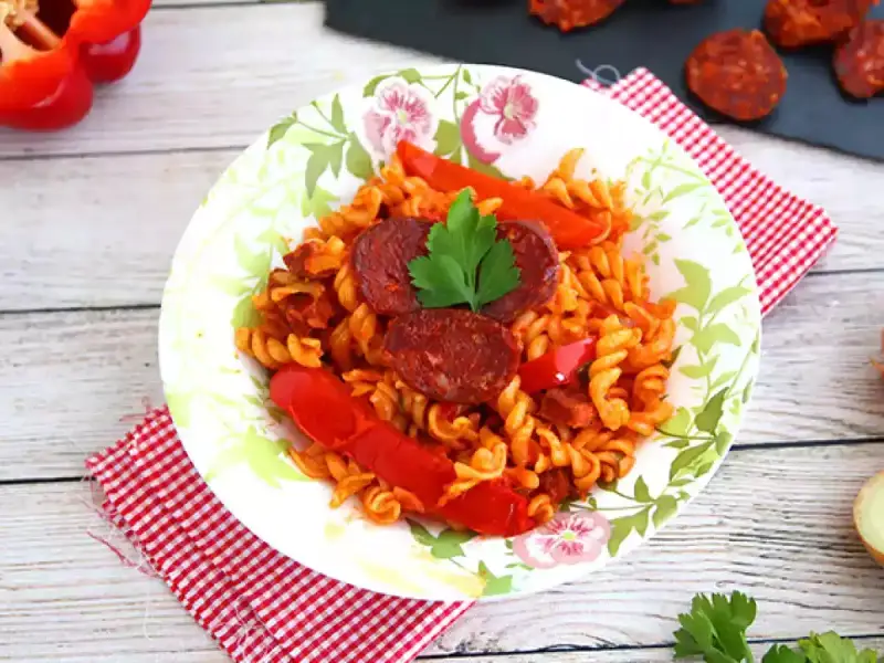Pyszny makaron z chorizo, papryką i natką pietruszki na talerzu z motywem kwiatowym.